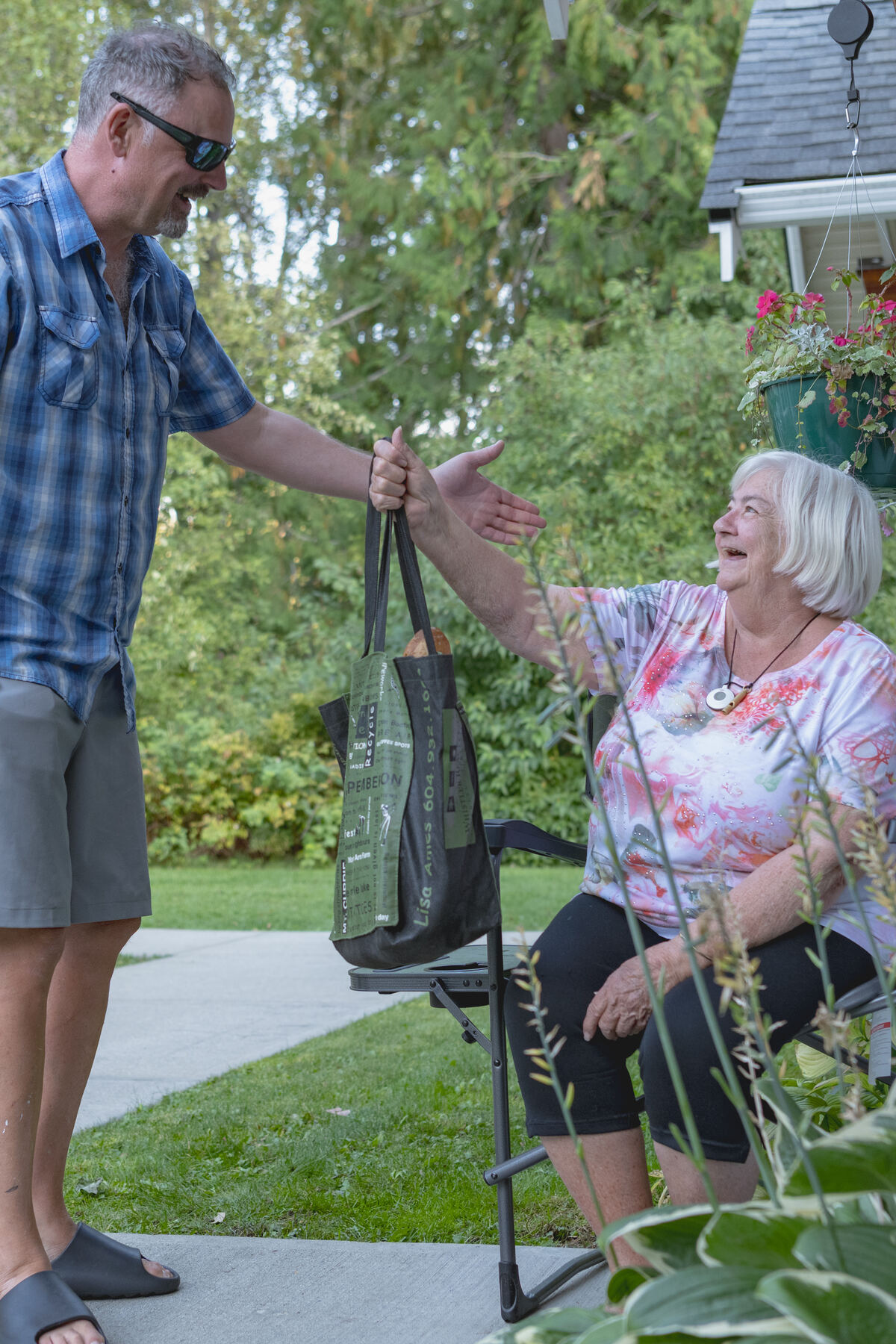 An Evergreen provider handing a bag of groceries to a laughing client outside her home